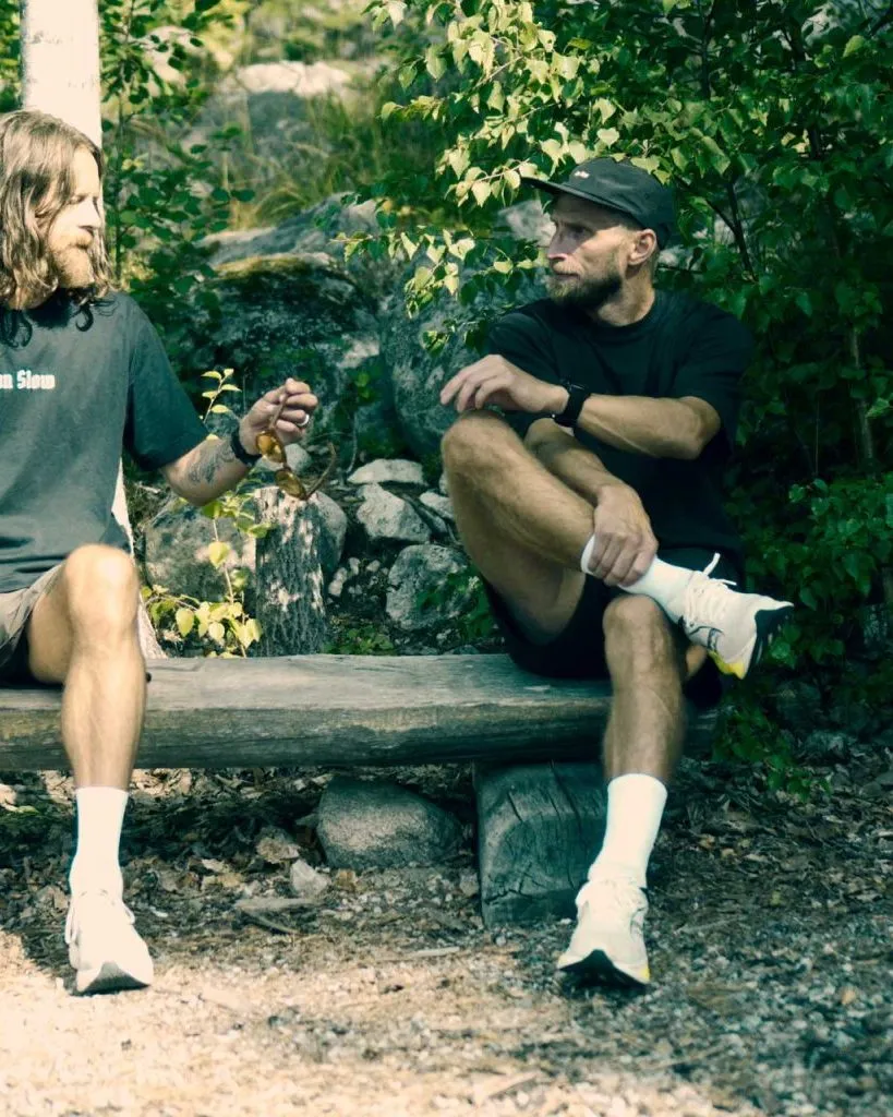 Two runners in Run Slow apparel sitting on a bench in the forest